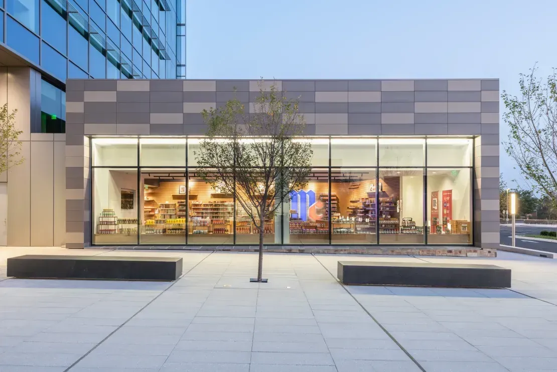 Grey fiber cement rainscreen panels above a glazed retail storefront — exterior cladding on a mixed-use building