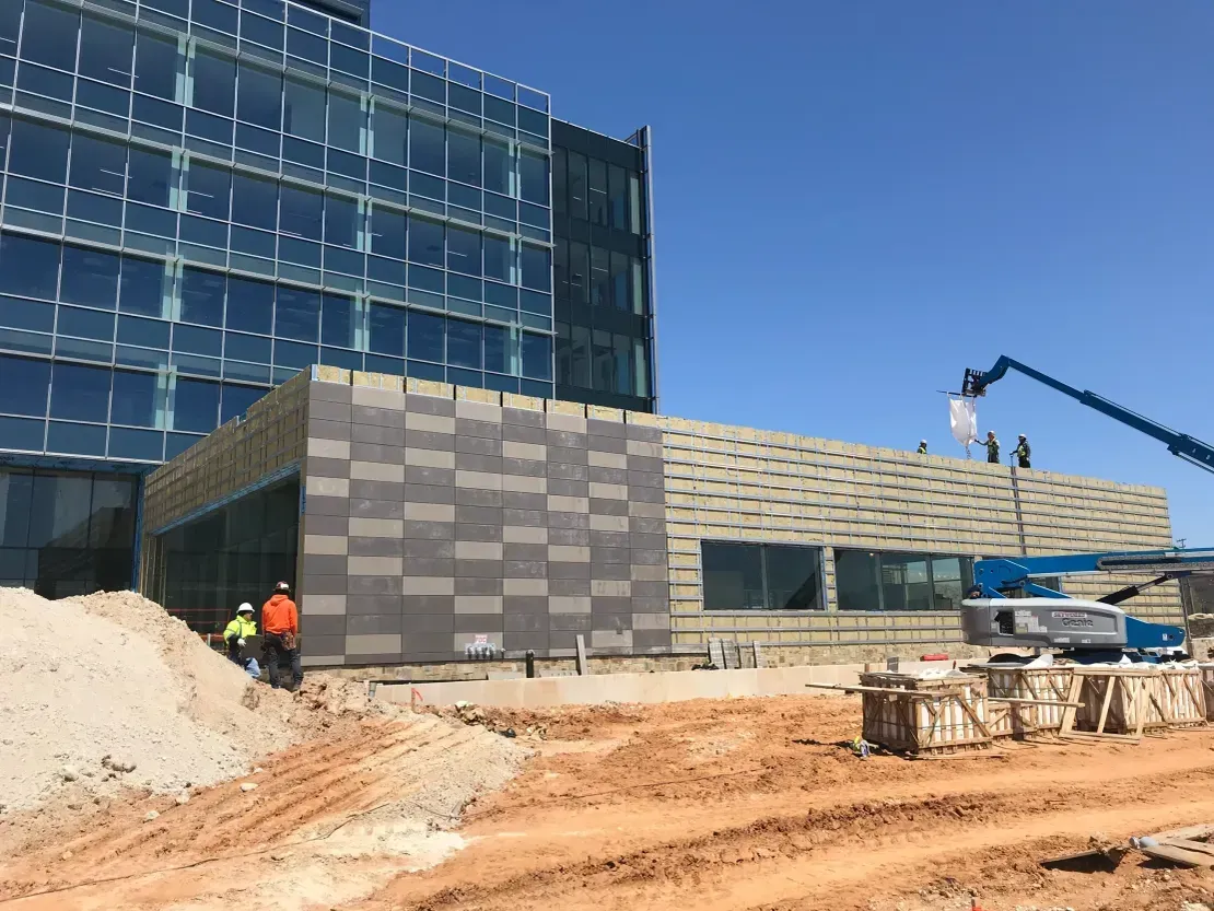 Rainscreen panel installation in progress on a commercial building with an aerial lift — exterior cladding and building envelope contractor serving Maryland, Virginia and DC